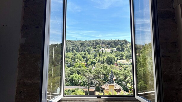 Una ventana ofrece una vista despejada de un paisaje verde y un edificio con techo puntiagudo.