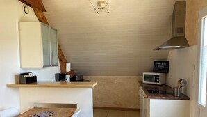 A compact kitchen with a wooden table, white chairs, a microwave, and a coffee maker. - Studio à la Campagne. Situé à 25 Minutes des Plages de Pénestin, Damgan (Missillac)