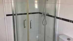 A glass-enclosed shower with a white toilet and a black mat in a bathroom with white tiles and black borders. - Studio à la Campagne. Situé à 25 Minutes des Plages de Pénestin, Damgan (Missillac)