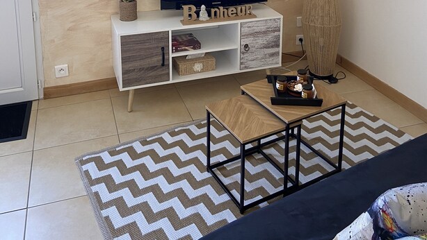 A modern living room with a sloped ceiling, a flat-screen TV on a wooden console, a patterned rug, and a black sofa. - Studio à la Campagne. Situé à 25 Minutes des Plages de Pénestin, Damgan (Missillac)