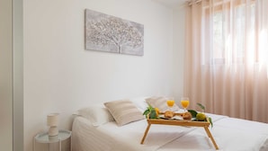 A neatly made bed with a tray of breakfast, a bedside lamp, and a painting of a tree on the wall. - Garden Vista Apartment (Dubrovnik)