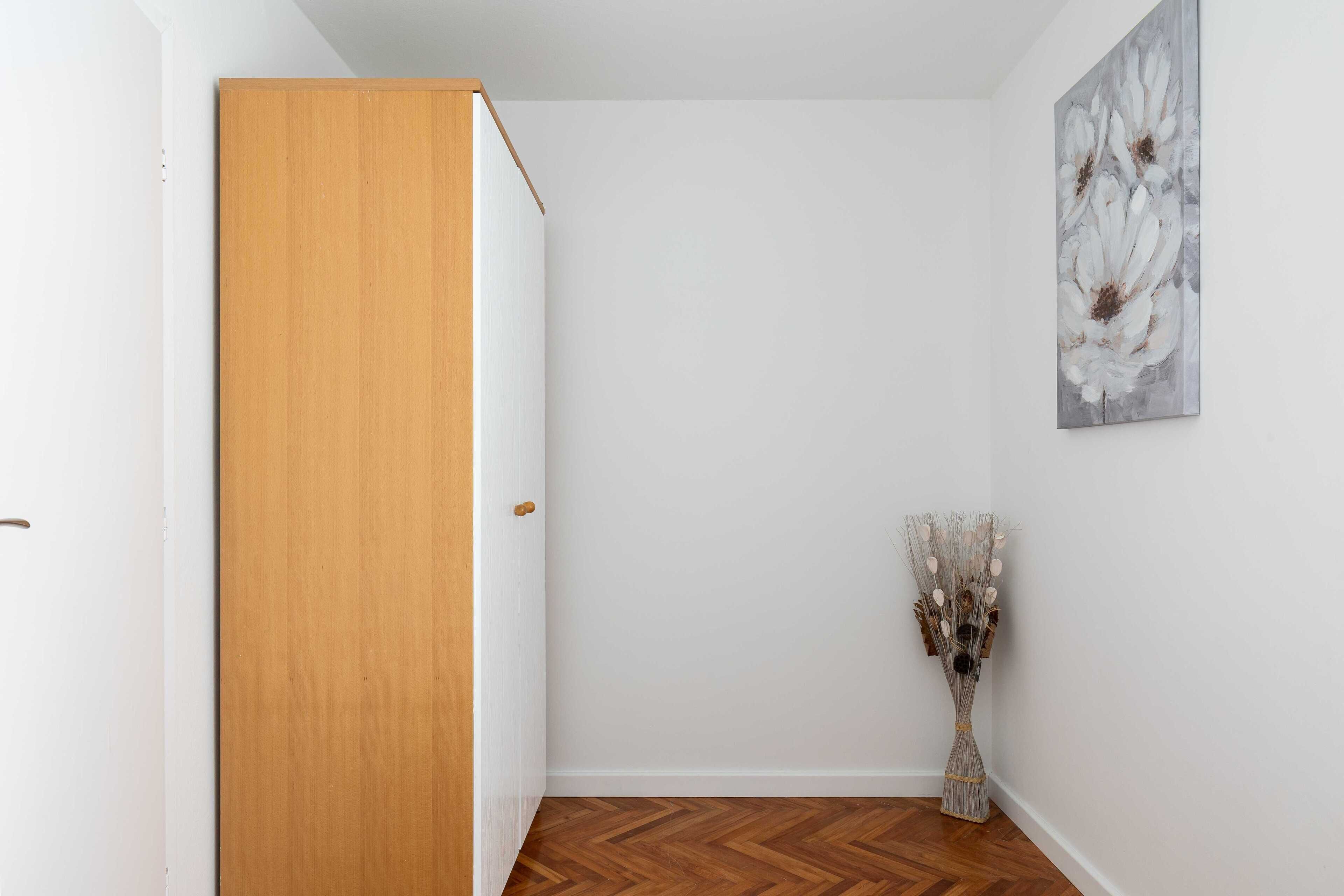 A hallway with a wooden door, a white wall, and a painting of flowers.