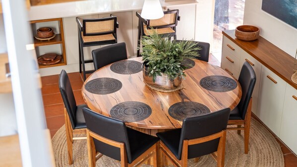 Una mesa de madera redonda con sillas negras, una planta en el centro y posavasos negros.