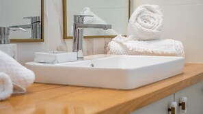 Un baño con un lavamanos blanco, grifo cromado y un espejo. Hay toallas blancas y un jabonera en la encimera.