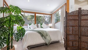 Ein Schlafzimmer mit Bett, großen Fenstern und einem dekorativen Holzschirm.