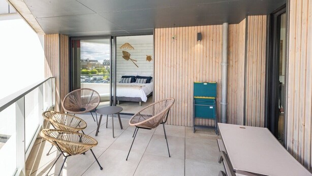 A balcony with wicker chairs, a small table, and a bed visible through the glass door.