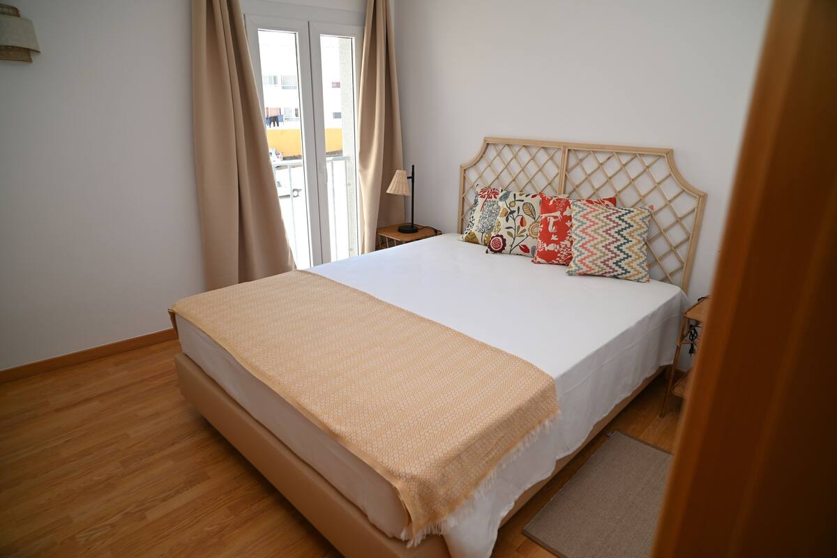 Un dormitorio con una cama grande, cabecera de madera y vistas a través de un ventanal.