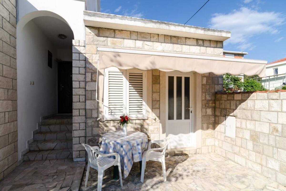 A stone building with a small patio area featuring a table and chairs, a door, and a window with shutters.