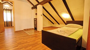 A bedroom with a wooden floor, a bed with a patterned bedspread, and a sloped ceiling with exposed beams. - Apartments Lemeš (Janjina)