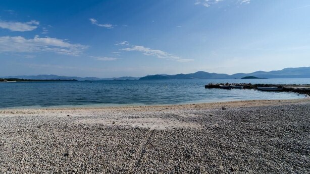 A pebbled beach with calm water and distant mountains under a clear sky. - Apartments Lemeš (Janjina)