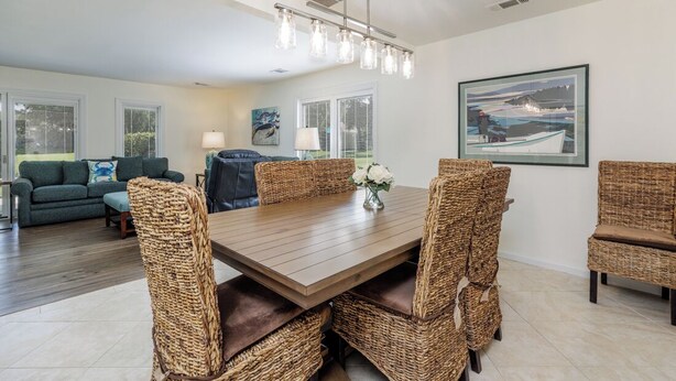 Un coin repas avec une table en bois et des chaises en osier, un lustre et des œuvres d’art accrochées aux murs.