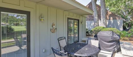 A covered patio with a round table and chairs, a covered grill, and a small garden area.
