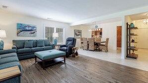 Un salon spacieux avec un ensemble de canapés, un coin repas avec des chaises en osier et une cuisine à l’arrière-plan.