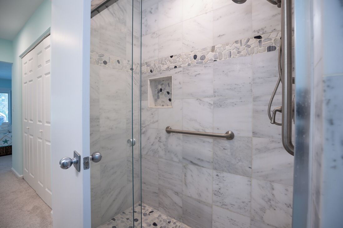 Een douche met glazen wanden, marmeren tegels en een handgreep.