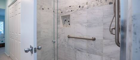 Een douche met glazen wanden, marmeren tegels en een handgreep.