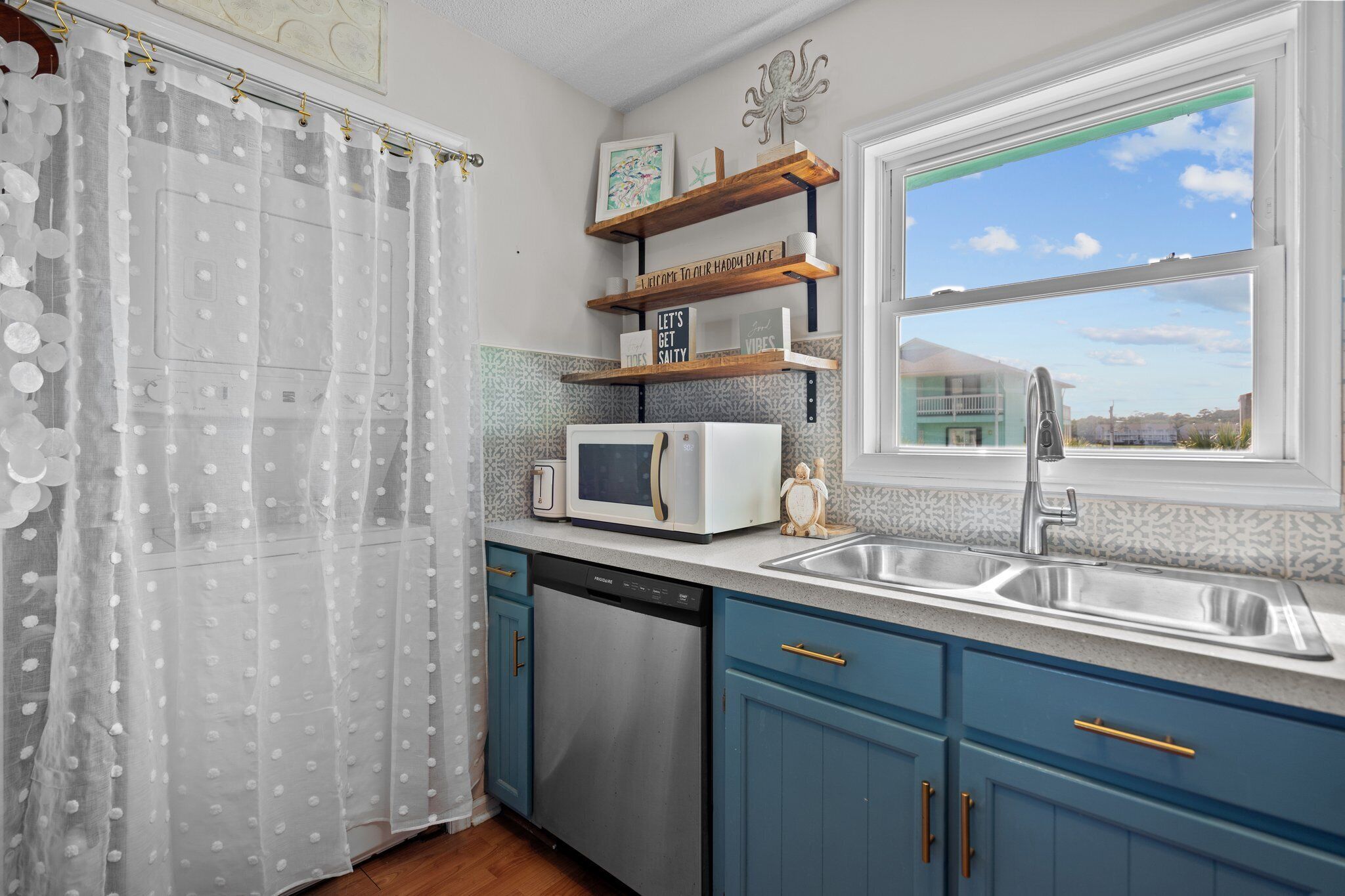 A kitchen with a dishwasher, a microwave, a sink, and a window with a view of a house.