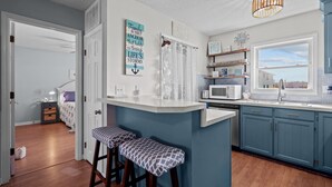 Une cuisine avec un mur d’accent bleu, un îlot central blanc et une vue sur l’extérieur.