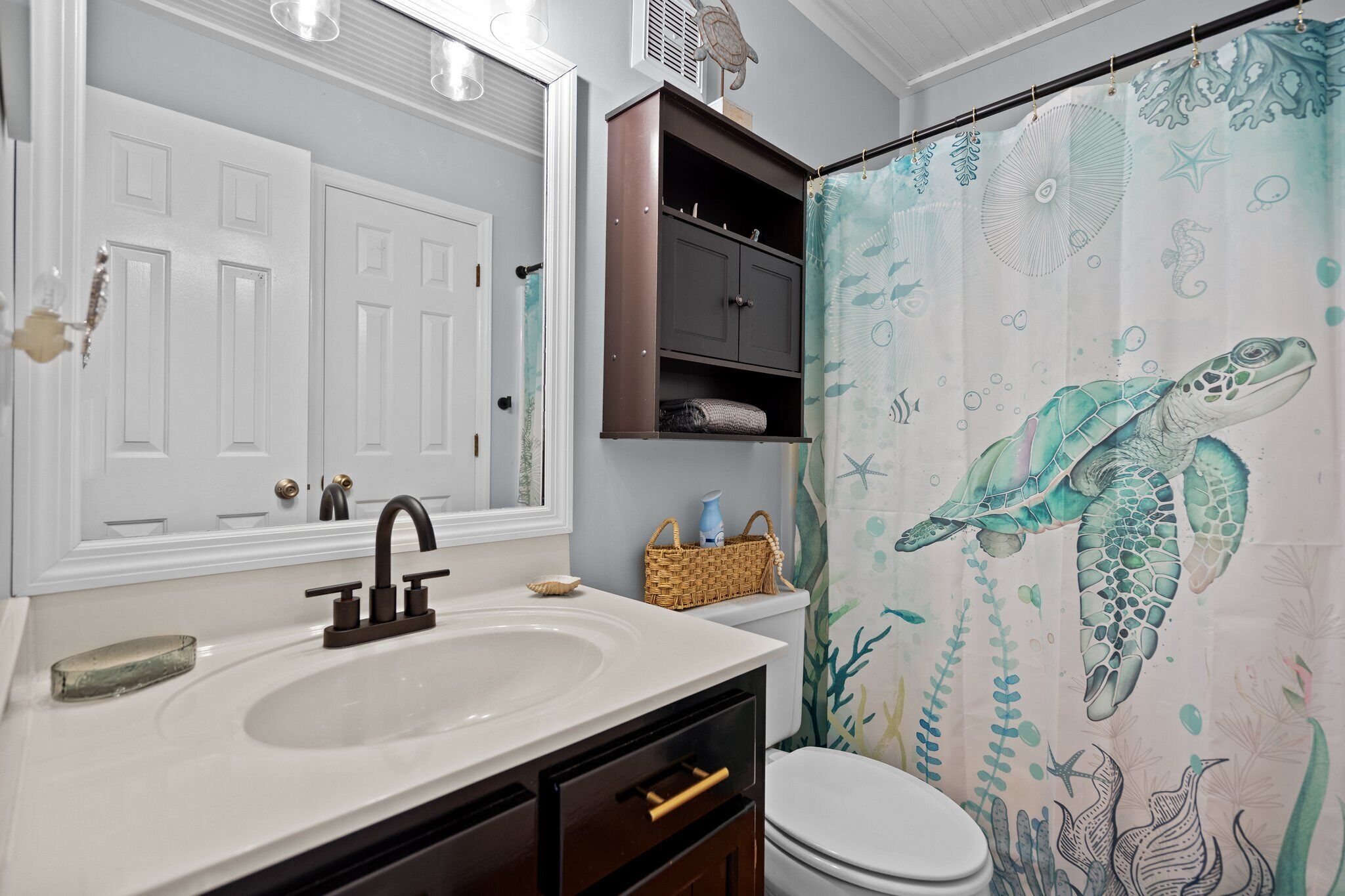 A bathroom with a white sink, dark cabinet, and a shower curtain with a sea turtle design.