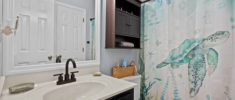 A bathroom with a white sink, dark cabinet, and a shower curtain with a sea turtle design.