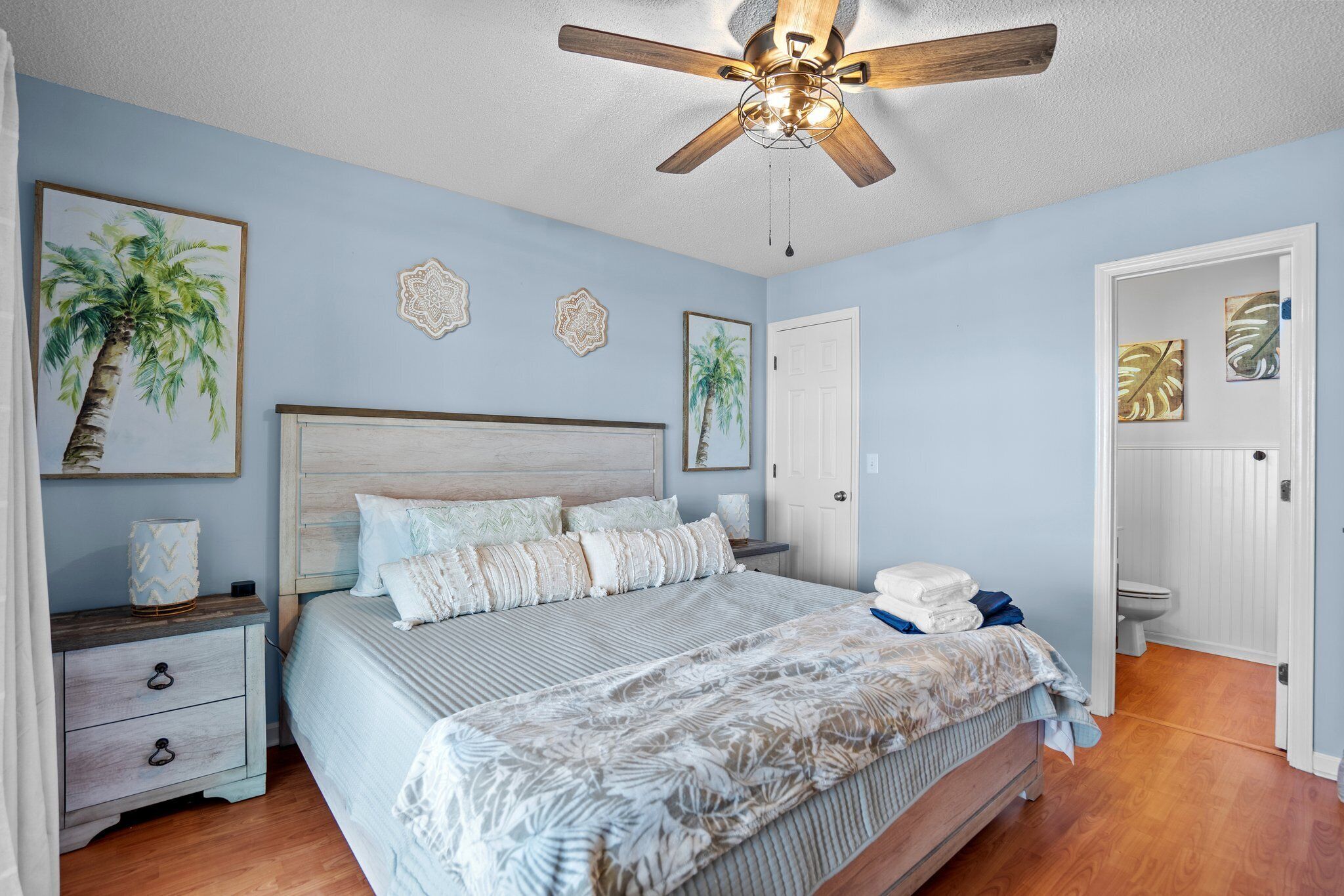 A bedroom with a bed, nightstands, a ceiling fan, and a door leading to a bathroom.