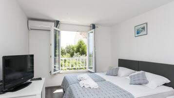 A hotel room with a bed, a TV, a desk, and a balcony with a view of greenery.