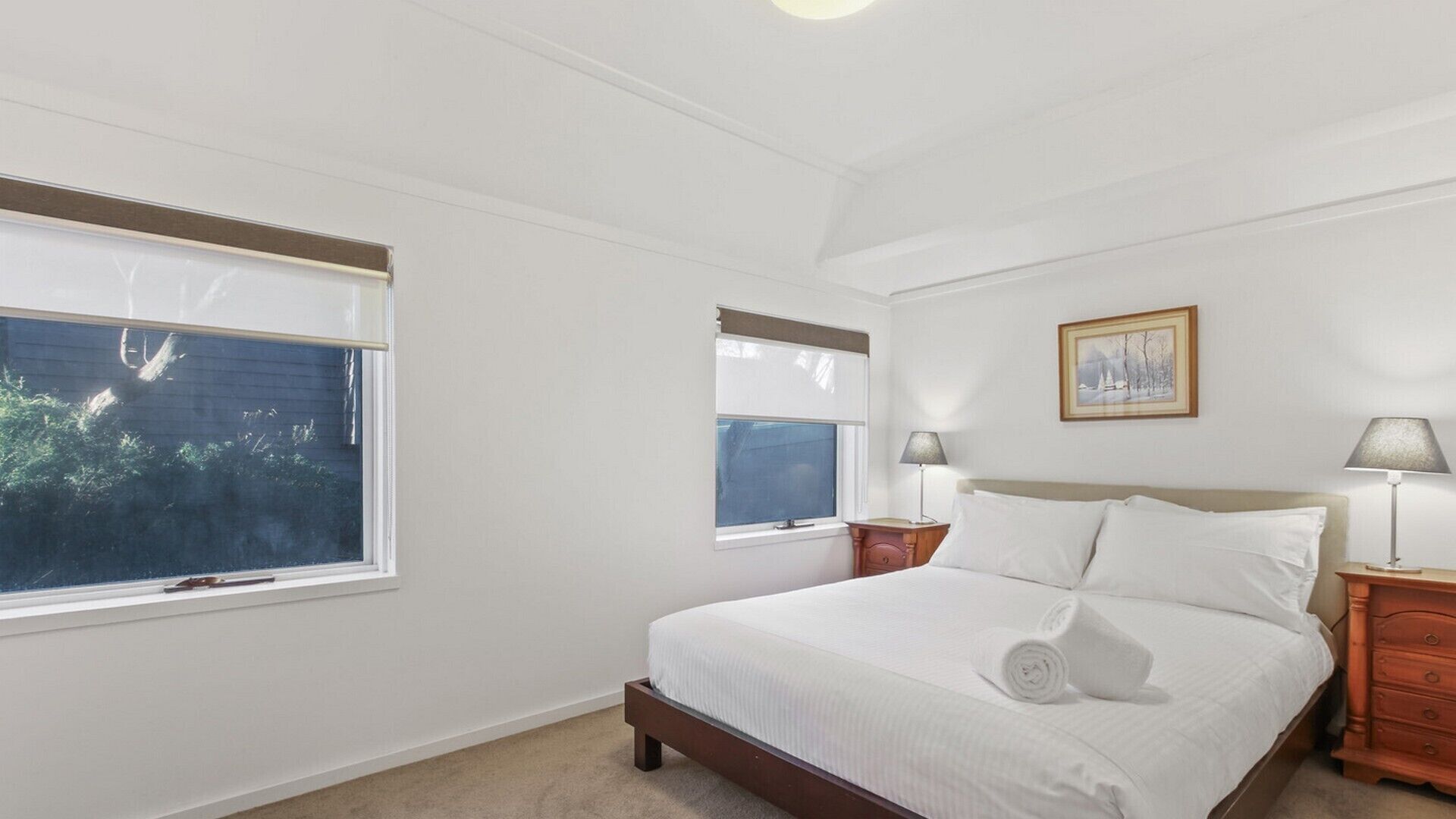 Un dormitorio con cama, dos mesitas de noche, una ventana y un cuadro enmarcado en la pared.