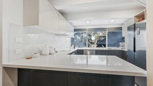 A modern kitchen with a large island, stainless steel appliances, and a view of the outside.
