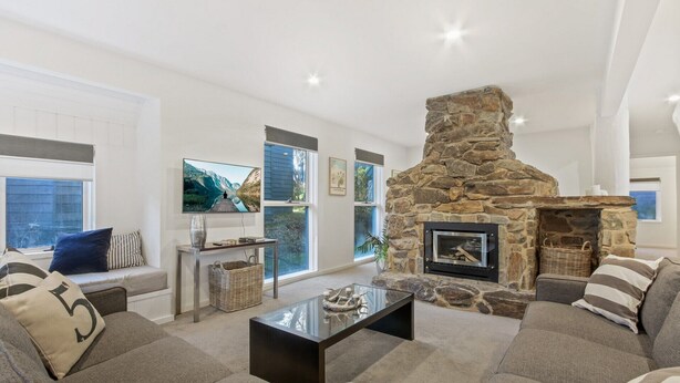 A modern living room with a stone fireplace, comfortable seating, large windows, and artwork on the walls.