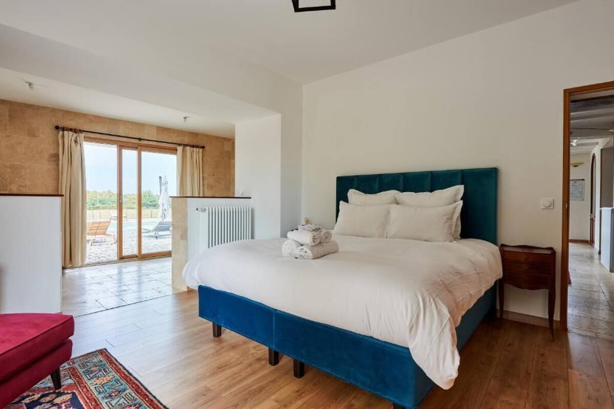 A bedroom with a large bed, a red chair, a wooden floor, and a view of the outdoors through a sliding door.