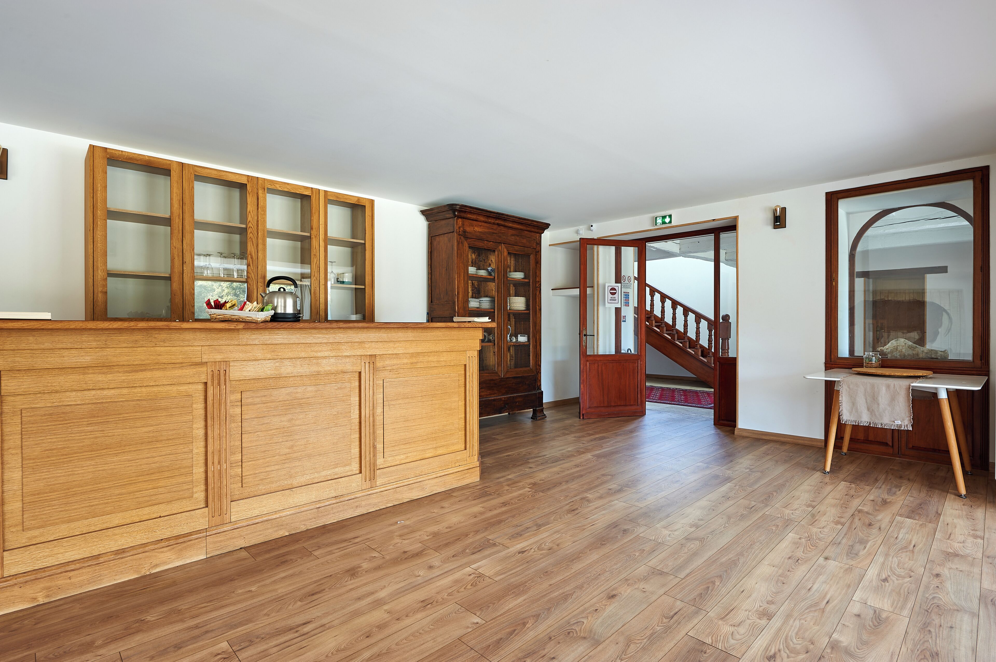 Een ruime keuken met houten kastjes en een centraal eiland. Een trap leidt naar een hoger gelegen verdieping, en een grote spiegel is aan de muur bevestigd.