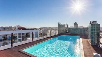 A rooftop pool with clear blue water, surrounded by a wooden deck and glass railings.