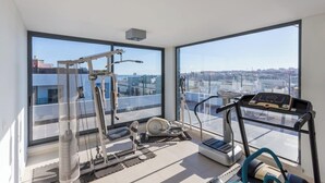 Een ruime kamer met grote ramen, een loopband, een elliptische trainer en een roeimachine.