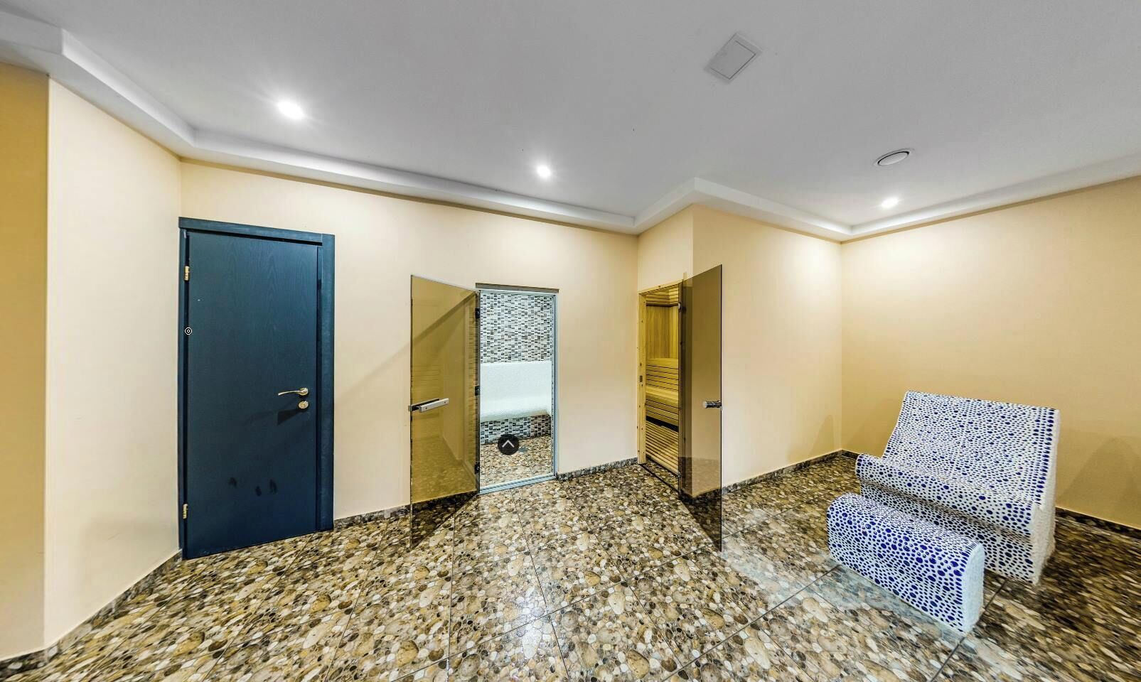 A hallway with a blue door, a glass partition, and patterned chairs.