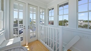 Um quarto claro e arejado, com amplas janelas, soalho de madeira e guarda-corpo branco.