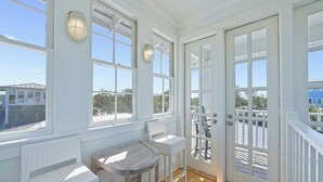 Quarto iluminado pelo sol com móveis de vime branco, janelas amplas e vista para o exterior.