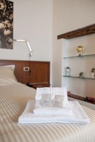 Una cama bien tendida con una toalla blanca doblada y dos botellas con la etiqueta "Nature" encima.
