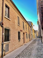 Una estrecha calle adoquinada flanqueada por edificios tradicionales de ladrillo, con diseños de ventanas uniformes y un cielo azul despejado.