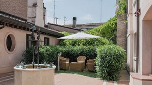 Une cour avec une fontaine, des chaises en osier et un grand parasol.