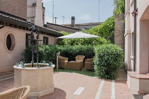 Un patio con una fuente, sillas de mimbre y un paraguas grande.