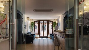 Un hall d’hôtel moderne avec une cloison en verre, un espace salon et une vue sur la rue.