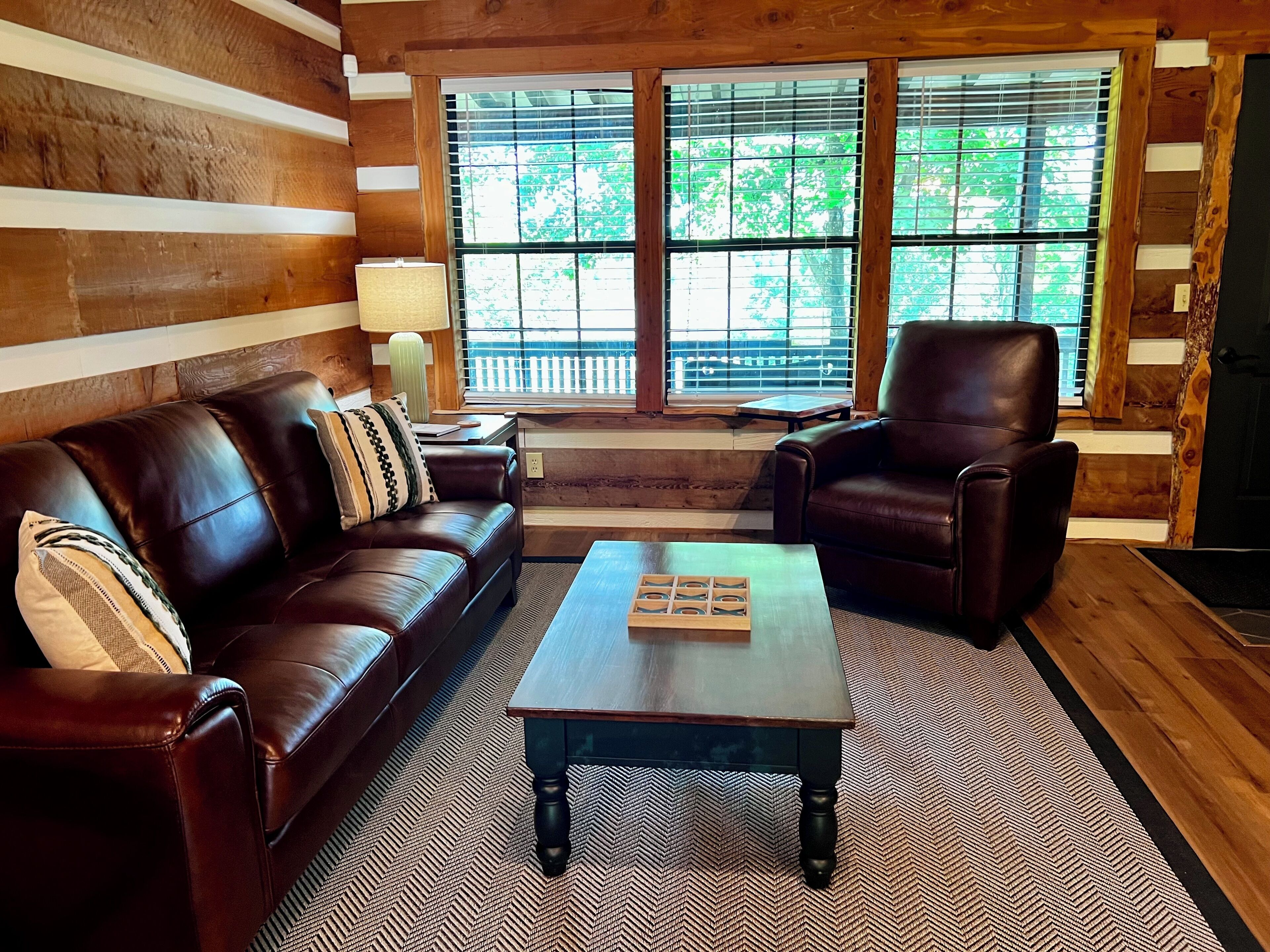 A log cabin interior with a brown leather sofa, a matching armchair, and a wooden coffee table.