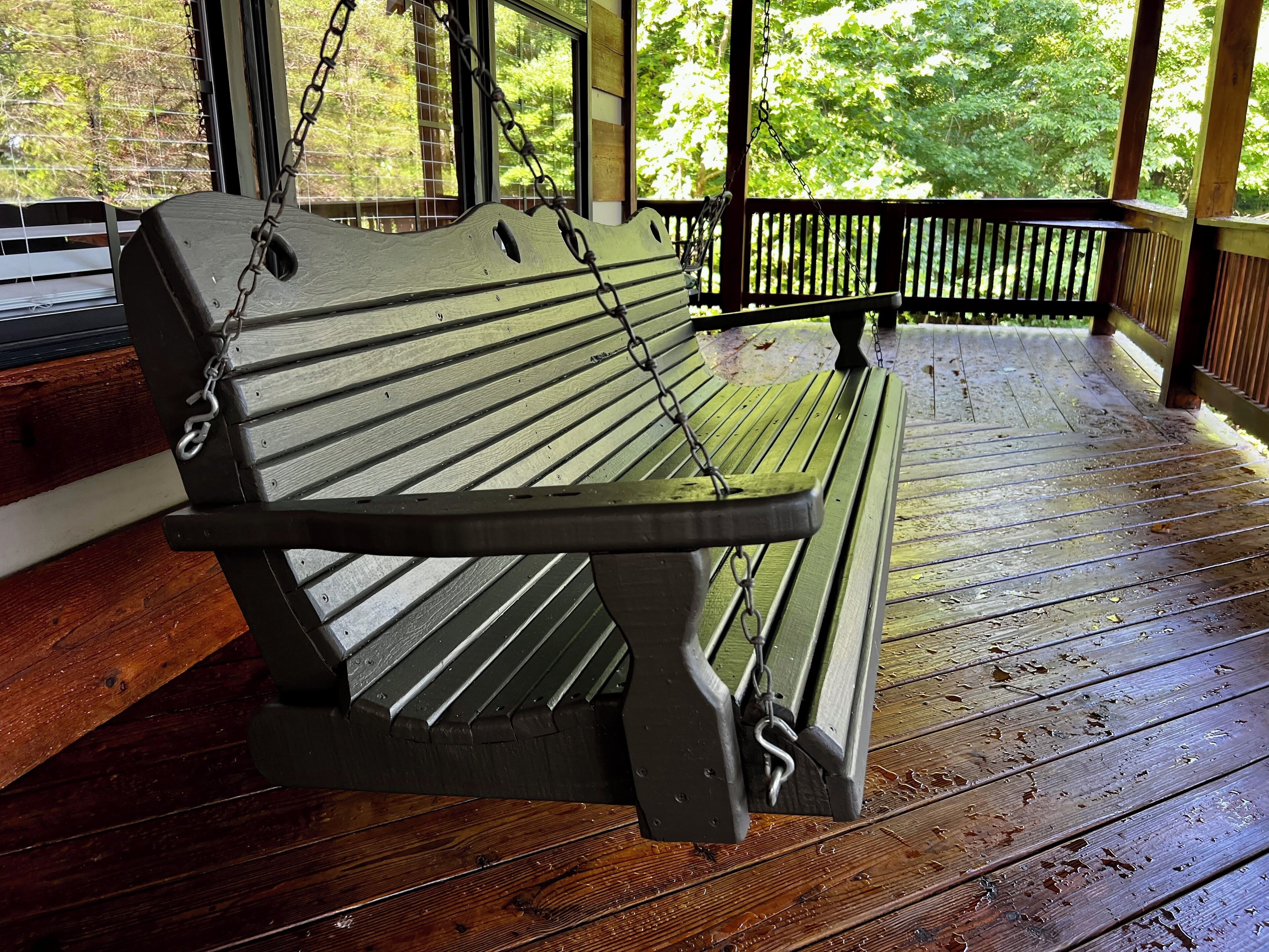 A wooden bench with metal chains, suspended on a wooden deck with a railing.