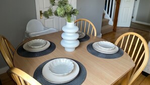 A dining table with four chairs, a white vase with greenery, and a staircase in the background. - Cozy Villa in Youghal, Co. Cork - Carleton Village  (Youghal)
