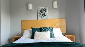 A neatly made bed with a green blanket, white and green pillows, and a wooden headboard. There are two bedside tables with lamps on either side of the bed. - Cozy Villa in Youghal, Co. Cork - Carleton Village  (Youghal)