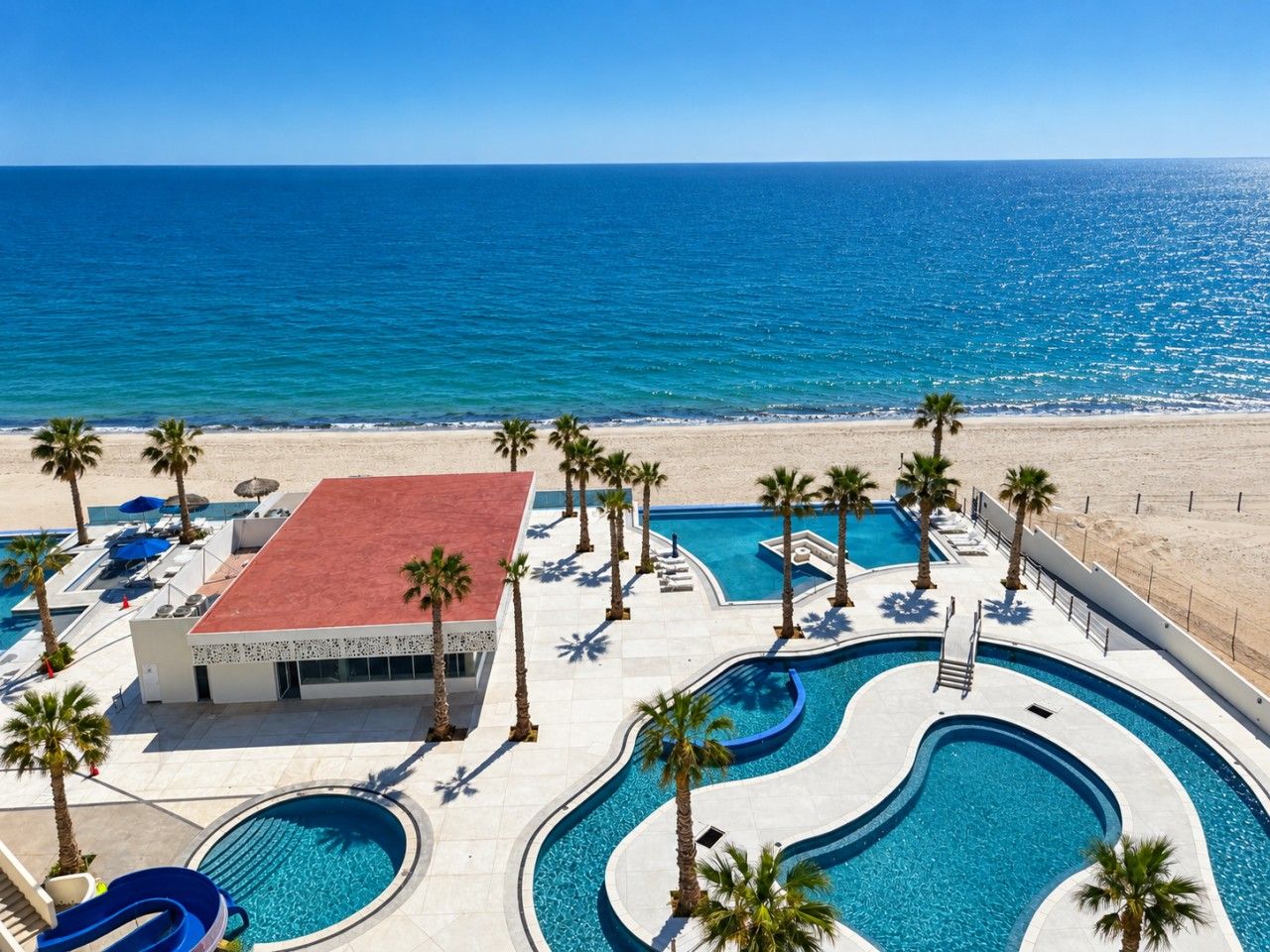 A resort with a swimming pool, palm trees, and a beach view.