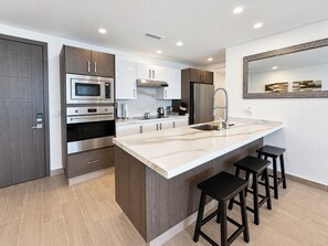 A modern kitchen with a central island, stainless steel appliances, and a large mirror above the sink.