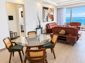 Uma sala de estar moderna com uma mesa de jantar de vidro, rodeada por cadeiras de vime, um sofá de couro e uma grande janela com vista para o oceano.