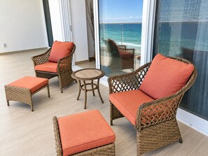 A balcony with wicker furniture, including chairs and a table, and a view of the ocean.