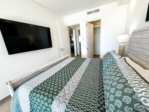 Ein Schlafzimmer mit einem Bett, einem an der Wand montierten Fernseher und einer Tür zu einem Badezimmer.