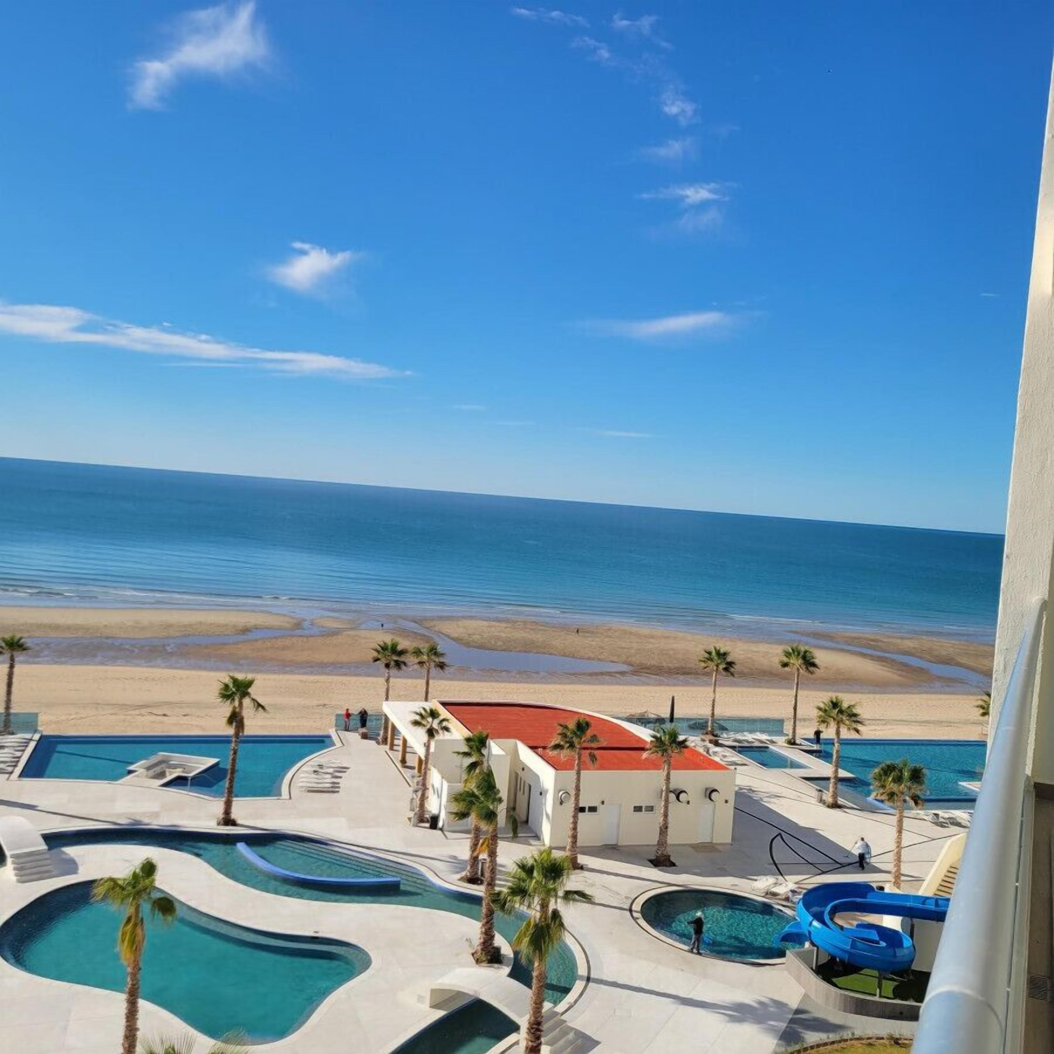 A resort with multiple swimming pools, palm trees, and a beach view.